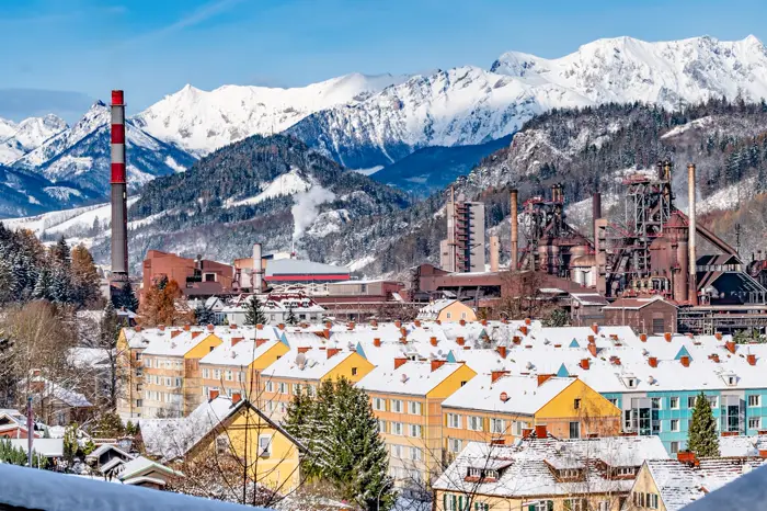 Snow covered rooftops and steelworks in Leoben, with mountains behind.